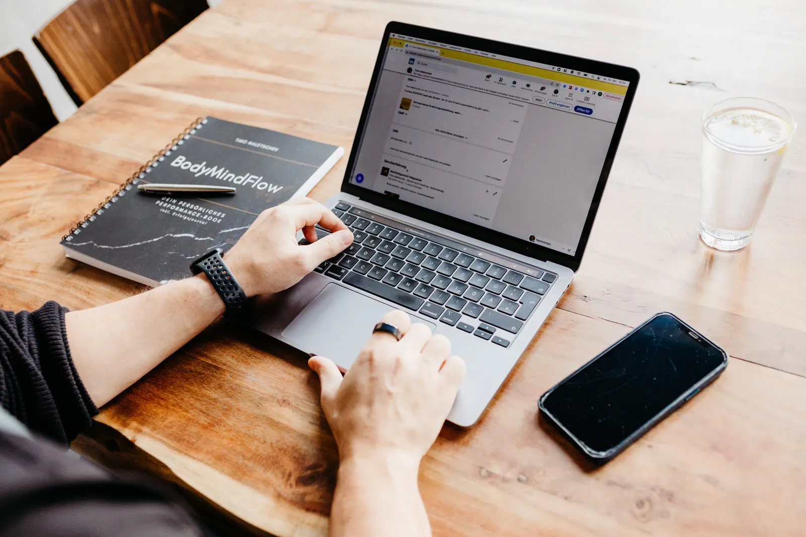 Laptop, Notizbuch, Smartphone und Wasserglas auf dem Schreibtisch von Timo Maletschek